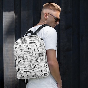 May include: White backpack with a black and white golf-themed pattern. The backpack features illustrations of golfers, golf courses, and the text "My Sporting Life Golf". The backpack has black shoulder straps and a top handle.