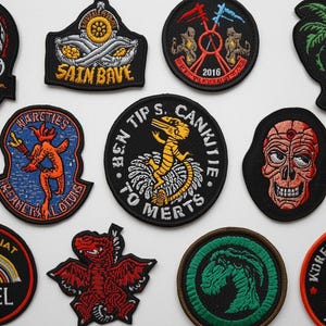 Puede incluir: Una colección de parches bordados con varios diseños. Incluye una calavera, un escudo con árboles, una palmera, un loro y otras formas únicas. Los parches presentan textos como "HALF WINE WEPARES" y "BEN TIPS S. CANKITIE TO MERTS".