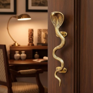Può includere: Una maniglia per porta in ottone a forma di cobra, fissata a una porta in legno marrone scuro. La maniglia presenta incisioni dettagliate ed è progettata per assomigliare a un serpente. È un elemento decorativo.
