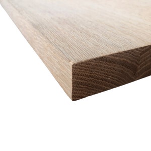 May include: Close-up of the edge of a light brown wooden board. The grain of the wood is visible.