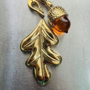 May include: A gold-tone acorn charm with a clear amber center and a gold-tone oak leaf charm.