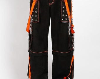 May include: Black pants with orange accents, featuring orange suspenders, studded details, and chain embellishments. The pants have a drawstring waist and are styled with black and white platform shoes. The stitching is orange.