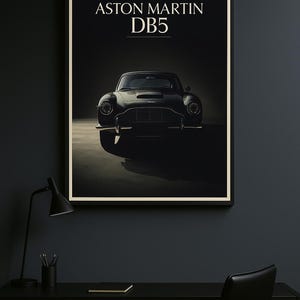 Può includere: Stampa incorniciata con un'Aston Martin DB5. L'auto è raffigurata in uno stile scuro e drammatico, con il testo "ASTON MARTIN DB5" in alto. La stampa è esposta su una parete scura sopra una scrivania nera.