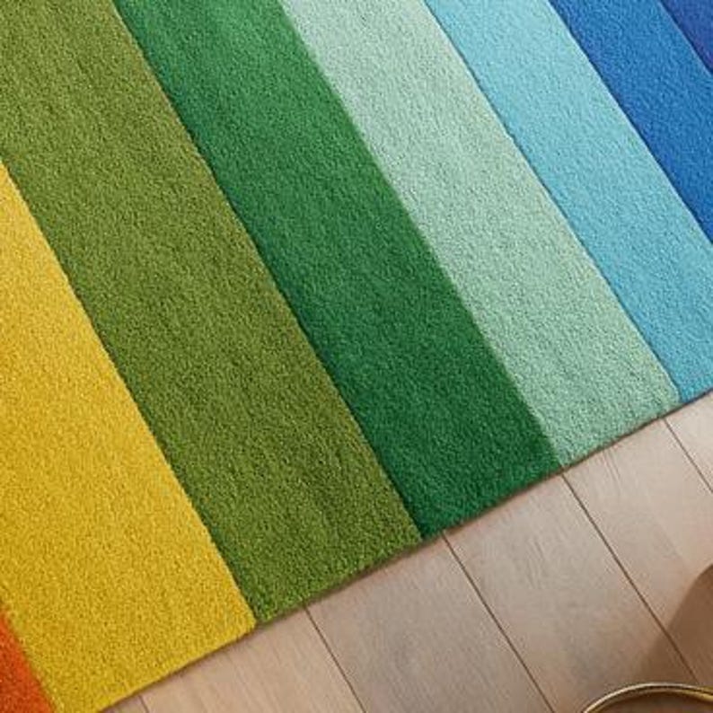 K&ouml;nnte beinhalten: Ein farbenfroher Teppich mit Regenbogenstreifen. Der Teppich hat gelbe, gr&uuml;ne, t&uuml;rkisfarbene, hellblaue und dunkelblaue Streifen. Der Teppich besteht aus einem weichen Material und liegt auf einem hellen Holzboden.