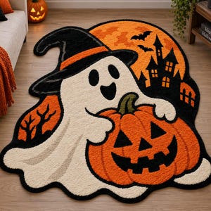 May include: A shaped area rug featuring a white ghost wearing a black witch hat with an orange band. The ghost holds a large orange jack-o'-lantern. The background displays a full orange moon, a black silhouette of a haunted house, and bats.