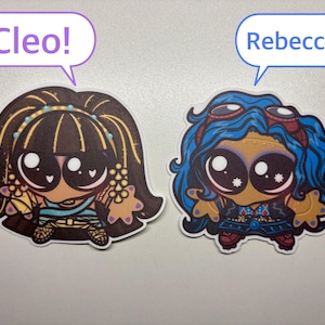 Op de afbeelding: Twee gestanste stickers met gestileerde stripfiguren met grote ogen. De linker sticker toont een personage met donker haar en de tekst Cleo! in een tekstballon. De rechter sticker toont een personage met blauw haar en de tekst Rebecca! in een tekstballon.