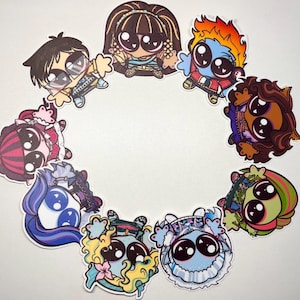 Op de afbeelding: Een verzameling van negen ronde stickers met gestileerde stripfiguren met grote zwarte ogen, gerangschikt in een cirkel. De figuren hebben diverse haarkleuren, waaronder bruin, oranje, blauw en roze, samen met verschillende outfits en accessoires.