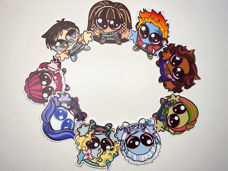 Op de afbeelding: Een verzameling van negen ronde stickers met gestileerde stripfiguren met grote zwarte ogen, gerangschikt in een cirkel. De figuren hebben diverse haarkleuren, waaronder bruin, oranje, blauw en roze, samen met verschillende outfits en accessoires.