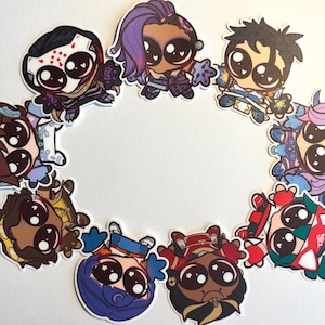 May include: A collection of colorful cartoon character stickers with large eyes, arranged in a circular pattern. Each sticker features a unique design with varying outfits and hairstyles, set against a white background.