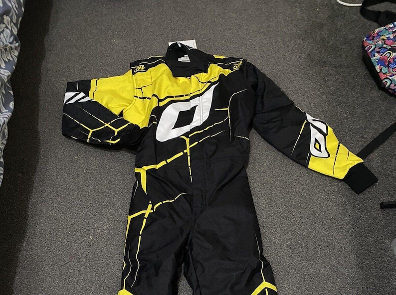 Pu&ograve; includere: Tuta da corsa nera e gialla con dettagli bianchi. La tuta presenta un design geometrico e il nome del marchio "OMP" in bianco. Ha maniche lunghe e una cerniera a tutta lunghezza. Realizzata in materiale resistente.