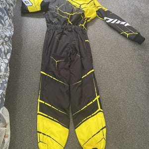 Pu&ograve; includere: Tuta da corsa nera e gialla con un design geometrico. La tuta presenta una base nera con dettagli gialli e un motivo giallo e nero sulla parte superiore del corpo e sulle gambe. Le maniche hanno testo bianco.