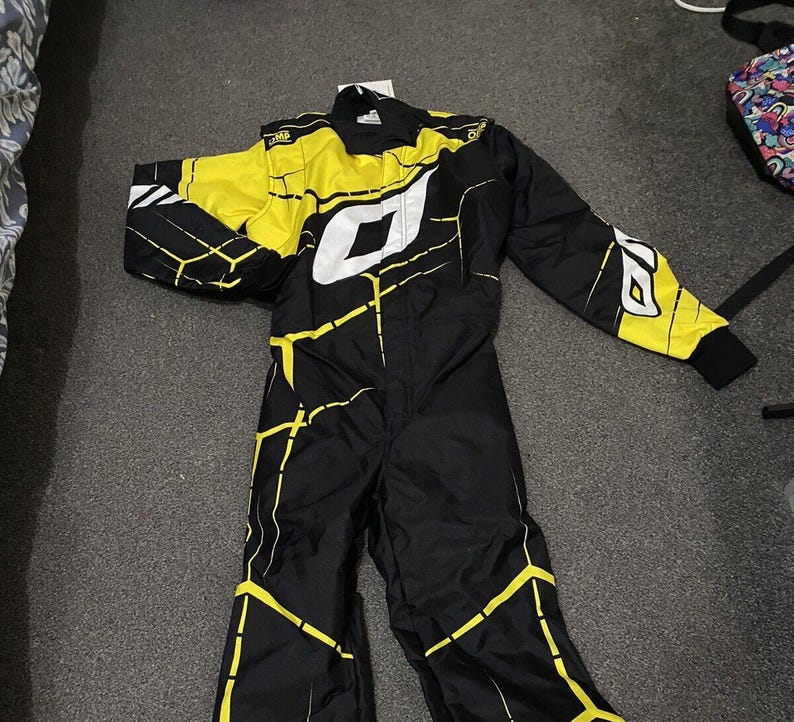 Pu&ograve; includere: Tuta da corsa nera e gialla con dettagli bianchi. La tuta presenta un design geometrico con linee gialle e un grande logo bianco sul petto. Le maniche e le spalle sono principalmente gialle, con polsini neri.