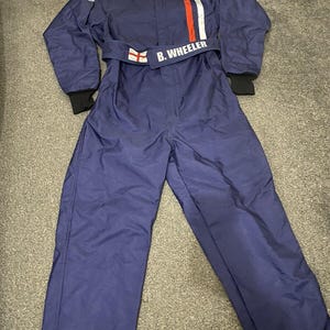 May include: A navy blue racing suit with white and red stripes on the chest. The suit has the name "B. Wheeler" on the belt and the OMP logo. The suit has black cuffs and white stripes on the shoulders.