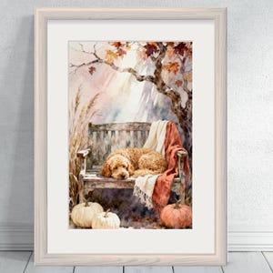 May include: Watercolour painting of a dog resting on a wooden bench, draped with a blanket. The scene is set in autumn, with pumpkins and fall foliage. The artwork is framed in a light-coloured wooden frame.