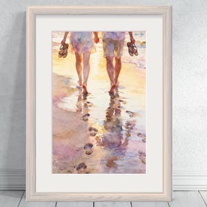 May include: Watercolour painting of two people walking barefoot on a beach at sunset. They are holding sandals and leaving footprints in the wet sand. The artwork is framed in a light-coloured wooden frame.