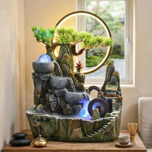 Peut inclure: Fontaine d'intérieur décorative avec un design de paysage miniature. La fontaine comprend une cascade, un petit pont et une roue à eau. Elle est éclairée par des LED bleues et vertes et possède une lumière circulaire au-dessus.