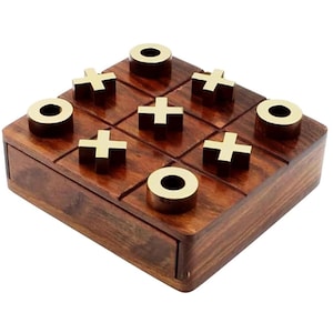 May include: A square wooden tic-tac-toe game board with a dark brown wood grain finish. The board features a grid of nine squares containing gold-colored metal game pieces in the shapes of X and O, arranged in a completed game pattern.