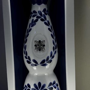 May include: Clase Azul tequila bottle in a white box. The bottle is white with blue floral designs and a silver emblem. The box has the brand name and "Mexico" printed on it.