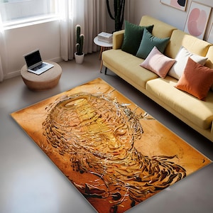 May include: A rectangular area rug with an abstract design in shades of brown and gold. The rug features a detailed, artistic rendering of a face. The rug is placed on a gray floor in a living room setting.