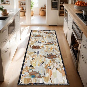 Op de afbeelding: Een rechthoekig keukenkleed met een mozaïekontwerp met theepotten. Het kleed heeft een witte achtergrond met verschillende vormen in tinten bruin, oranje en geel. De theepotten zijn bruin en blauw. Het kleed is afgezet met een donkerblauwe rand.