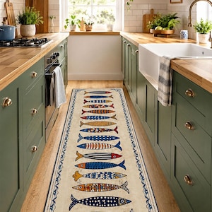 Könnte beinhalten: Ein langer, rechteckiger Küchenteppich mit cremefarbenem Hintergrund und einem sich wiederholenden Muster aus bunten Fischen. Die Fische sind in verschiedenen Farben und Designs gehalten, mit einem blauen Zierrand. Der Teppich liegt in einer Küche mit grünen Schränken und Holzarbeitsplatten.