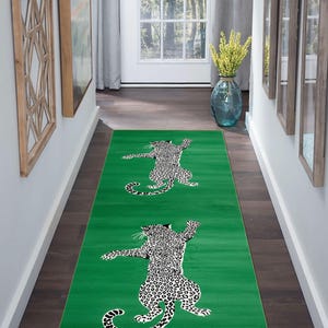 Puede incluir: Una alfombra verde con diseño de leopardo. La alfombra presenta un fondo verde brillante con un patrón repetido de un leopardo en blanco y negro. La alfombra es rectangular y está colocada en un pasillo.