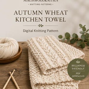 May include: A digital knitting pattern for an Autumn Wheat Kitchen Towel by Northwoodknitsus. The image shows a folded cream-colored knitted towel with a cable stitch design, a ball of yarn in a wooden bowl, and two wooden knitting needles.
