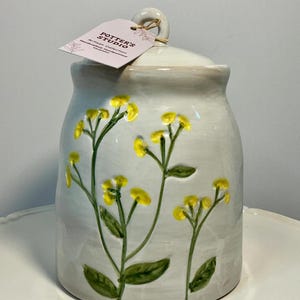 May include: A handmade wooden sign with the text "Welcome" in a playful font. The sign is painted white with a distressed finish, and features a decorative floral design in shades of pink and green. It is designed for indoor or outdoor use.