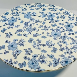May include: Round, cream-colored serving platter with a blue floral pattern. The design includes flowers and butterflies. The edge of the platter has a gold trim. This decorative piece is ideal for serving food.