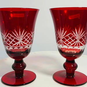 Puede incluir: Dos copas de vino tinto rubí con intrincados diseños de cristal tallado. Las copas presentan un cuenco acampanado, un tallo decorativo y una base redonda. El diseño de cristal tallado incluye un patrón de diamantes y estrellas.