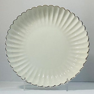 May include: A white ceramic plate with a scalloped edge and a silver trim. The plate has a ridged design radiating from the center. This elegant plate is suitable for serving food.