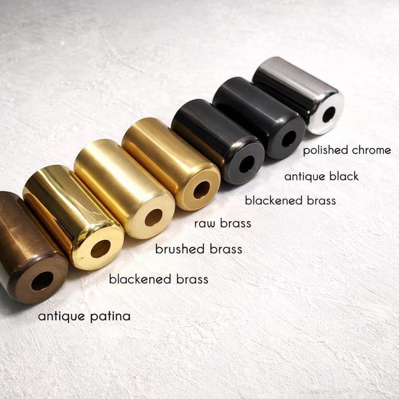 May include: An assortment of cylindrical metal objects in different finishes, such as polished chrome, antique black, and raw brass. Each cylinder has a hole at both ends. The text labels the finishes: antique patina, blackened brass, brushed brass.
