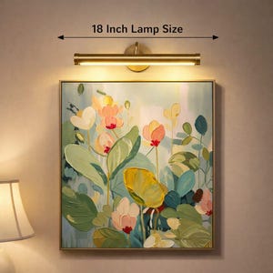 May include: A brass picture light, 45.7 cm in length, shines on a floral painting. The artwork displays flowers in pink, yellow, and green hues. The painting, framed in gold, is mounted on a neutral wall.