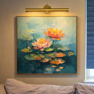 May include: A framed painting shows two orange and pink lotus flowers with lily pads, set against a teal background. A gold picture light shines on the artwork. The painting is above a sofa. The artwork is approximately 60 cm x 60 cm.