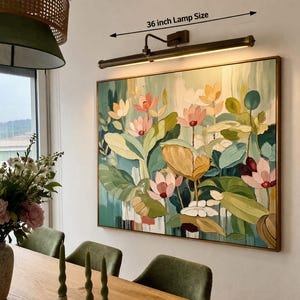 May include: A framed floral painting with a 91 cm lamp above it. The artwork features pink, yellow, and white flowers with green leaves. The lamp has a bronze finish and is mounted on the wall. The painting is in a wooden frame.