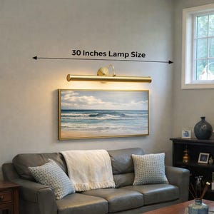 May include: A gold-toned picture light, measuring 76 cm, is positioned above a framed seascape. The lamp provides illumination to the artwork, enhancing the room's decor. The text "30 Inches Lamp Size" is displayed above the lamp.