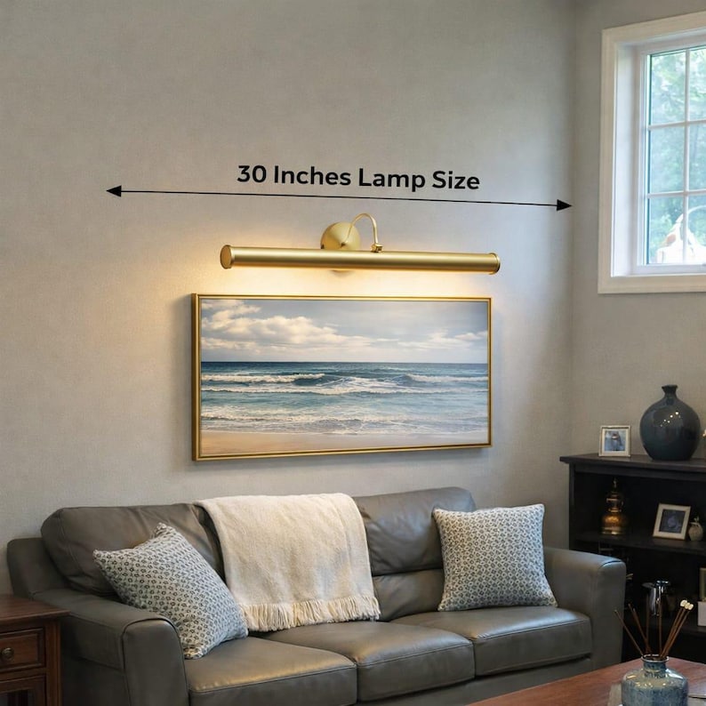 May include: A gold-toned picture light, measuring 76 cm, is positioned above a framed seascape. The lamp provides illumination to the artwork, enhancing the room's decor. The text "30 Inches Lamp Size" is displayed above the lamp.
