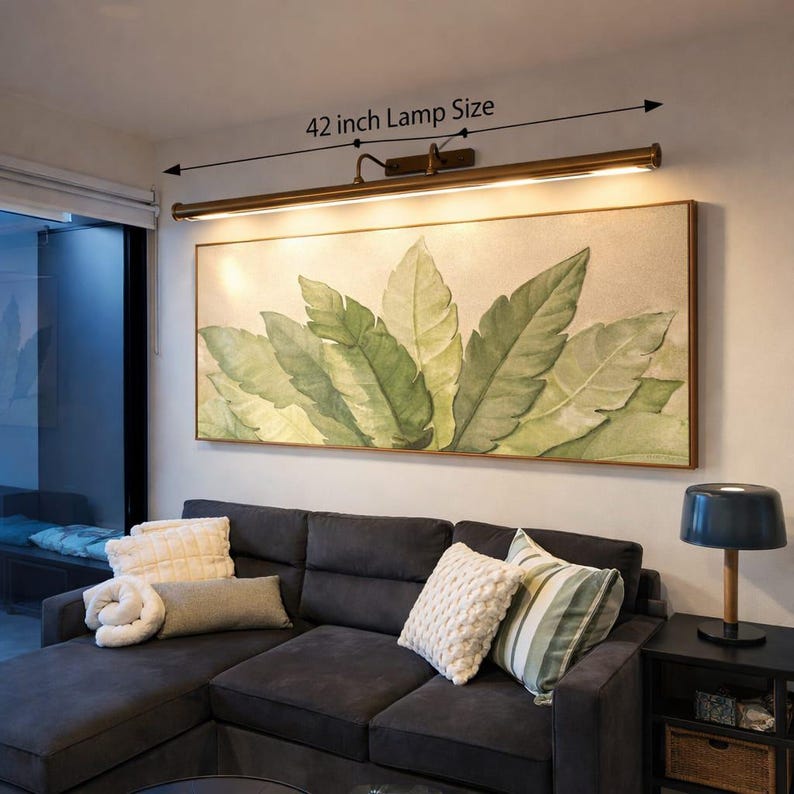 May include: A 107 cm bronze picture light fixture mounted above a large rectangular wall art piece featuring a botanical print of green leaves on a light background. The lamp provides illumination over the artwork.