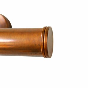 May include: A close-up shot of a copper-coloured cylindrical object with a rounded end. The object has a smooth, polished surface and appears to be made of metal. The end features three concentric rings. The background is plain white.