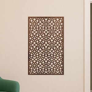May include: A dark brown wooden wall panel with a geometric starburst design. The panel is mounted on a beige wall. The room also features a green armchair, a teal ottoman, and a wooden toy. The panel measures approximately 60 cm x 100 cm.
