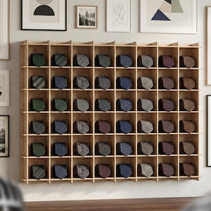 Könnte beinhalten: Ein wandmontierter Organizer aus hellem Holz mit einem Raster aus achtundvierzig quadratischen Fächern, in denen jeweils eine gefaltete Krawatte in verschiedenen Farben und Mustern, darunter Grün, Blau, Grau, Braun und Violett, liegt.