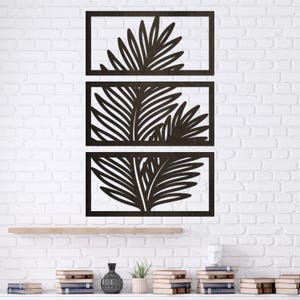 May include: A set of three rectangular wall art panels featuring dark brown laser-cut palm leaf silhouettes. Each panel is framed in a matching dark brown border, displaying intricate botanical foliage patterns arranged in a vertical stack.