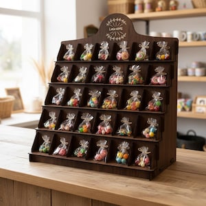 May include: A dark brown wooden display stand filled with small clear bags of colorful candies. The stand has multiple shelves, each holding several bags of treats. The top of the stand has a decorative design with the text "Logo Name".