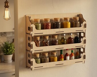 Könnte beinhalten: Ein dreistöckiges, an der Wand montiertes Gewürzregal aus hellem Holz mit verschiedenen Glasbehältern, die mit bunten Gewürzen, getrockneten Kräutern und kleinen Flaschen mit flüssigen Würzmitteln gefüllt und mit Kork- oder Schraubverschlüssen versehen sind.