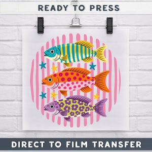 May include: A white print featuring three colourful fish with striped, polka-dot, and patterned designs, set against a pink striped background. The text "READY TO PRESS" and "DIRECT TO FILM TRANSFER" are at the top and bottom.