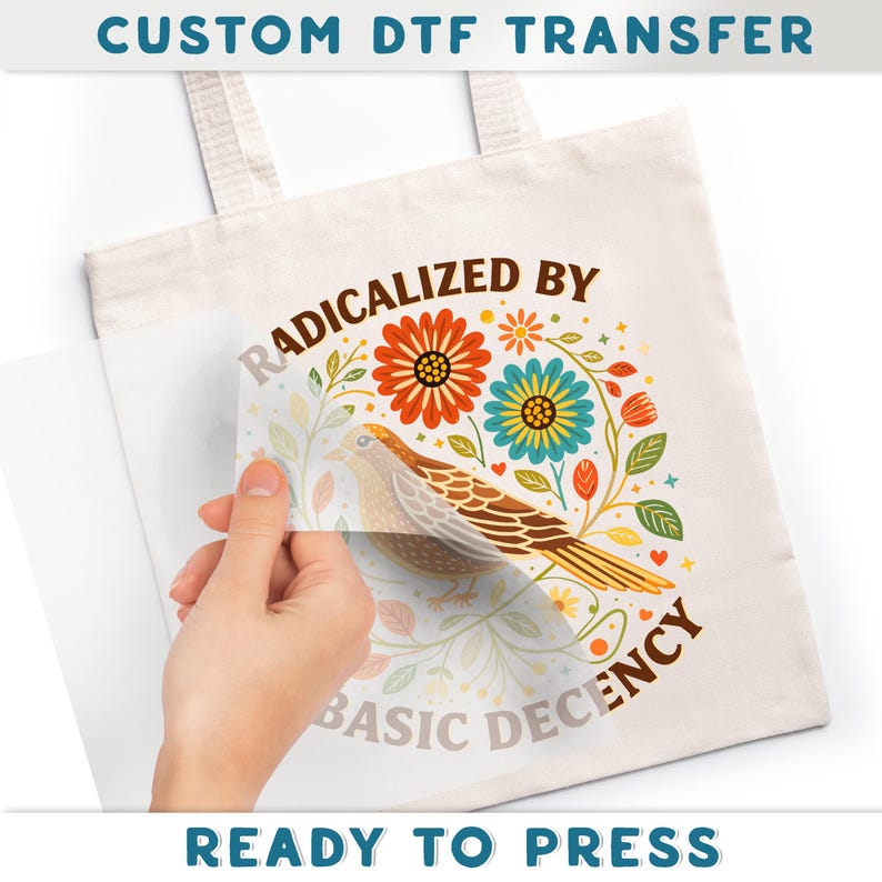 A hand is holding a white tote bag with a colorful floral design and the text "RADICALIZED BY BASIC DECENCY" printed on it.