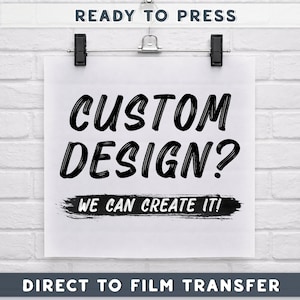 May include: A white paper with the words "CUSTOM DESIGN? WE CAN CREATE IT!" in black brush lettering, held by clips against a white brick wall. The text "READY TO PRESS" and "DIRECT TO FILM TRANSFER" are also visible.