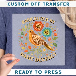 a person holding a clear plastic sheet with a colorful illustration of a bird surrounded by flowers and leaves.