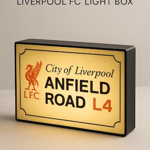 Könnte beinhalten: Schwarze Leuchtbox mit der Aufschrift "ANFIELD ROAD L4" in großen Buchstaben, dem Logo des Liverpool FC und "City of Liverpool". Der Artikel ist dekorativ, für Fußballfans.
