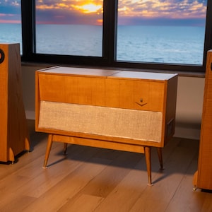 Puede incluir: Un mueble consola de madera estilo mediados de siglo con una rejilla de altavoz de tela clara y un pequeño detalle metálico en forma de V, flanqueado por dos altavoces de suelo de madera altos y delgados con conductores circulares cobrizos.